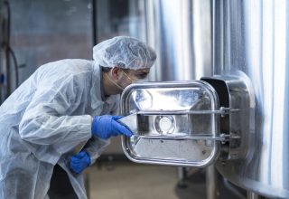 Technologist in white suit looking inside machine in food factory production line.